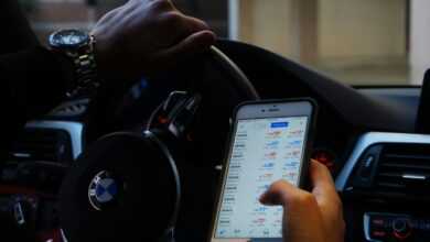 Person using mobile phone for currency trading while driving BMW car.