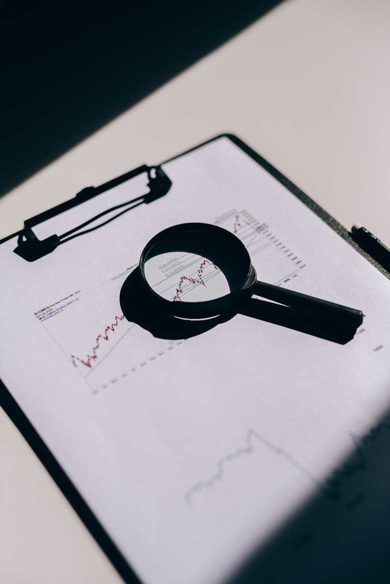 Detailed close-up of financial documents with graphs and magnifying glass on a clipboard.