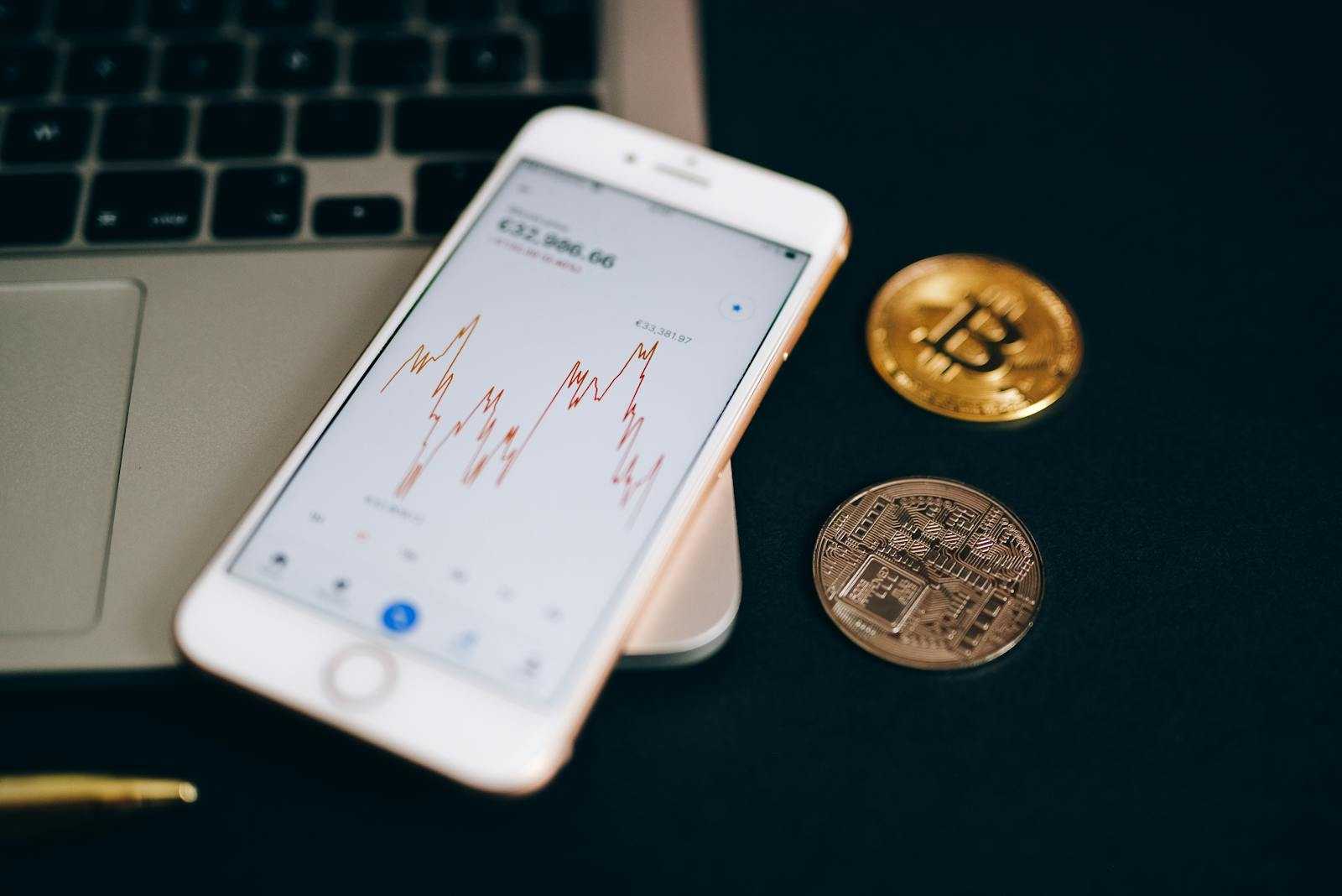 Close-up view of cryptocurrency coins and stock market graph on a smartphone screen.